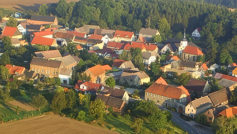 Stilisierte Illustration von Prießnitz mit Kirche und Dorfhäusern